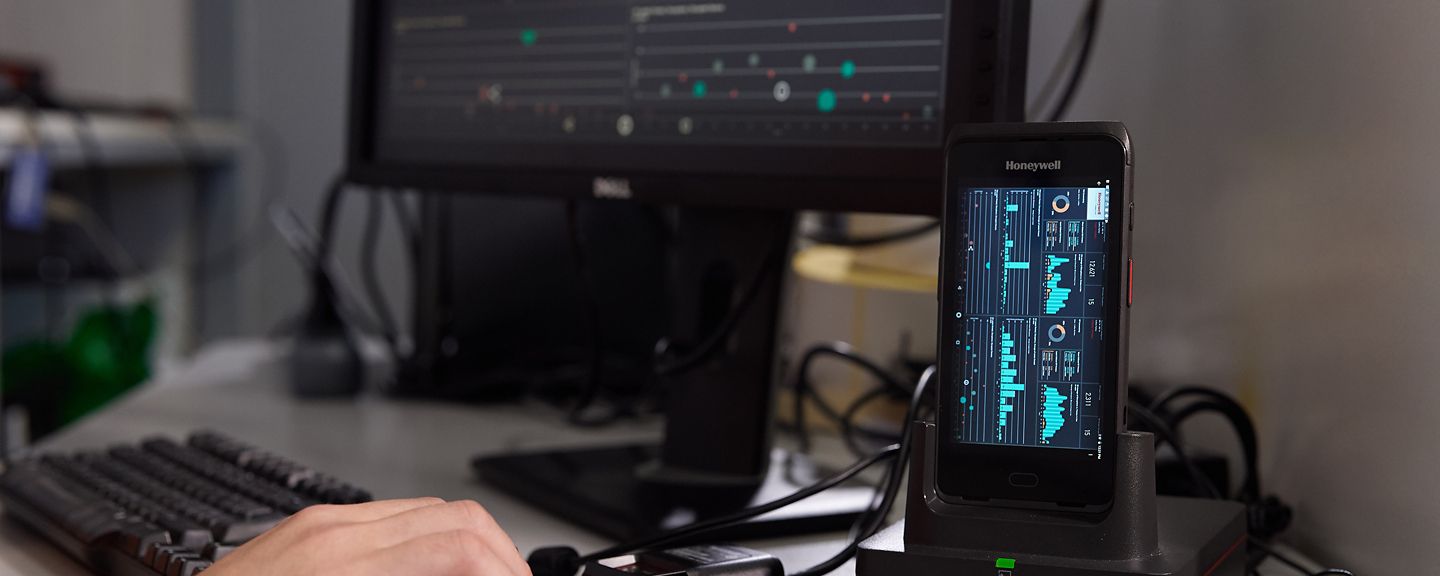 hand on a mouse next to a keyboard and a honeywell device