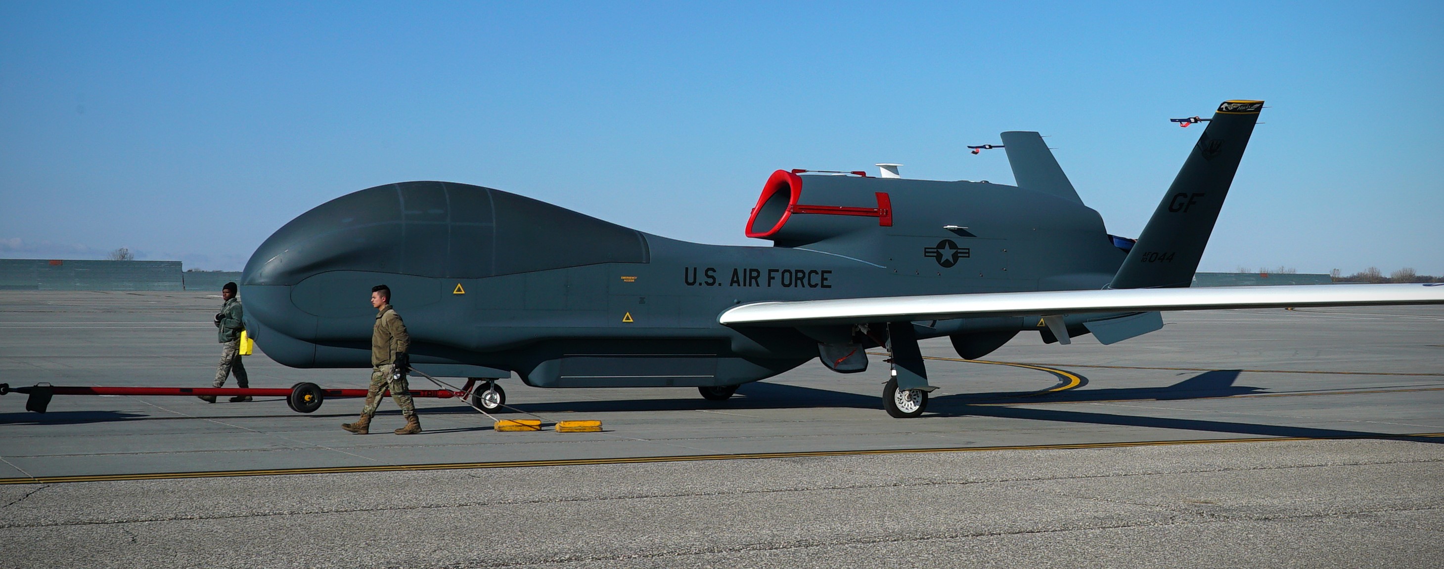 An aircraft sits on the flightline while two Airmen walk beside it.