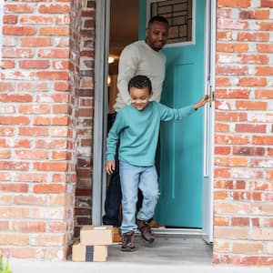 A father and his son exiting a brick house