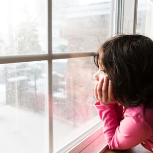 A child looks at snow outside window
