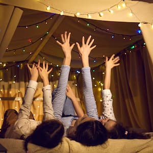 A mother laying with her children in a tent decotared with Christmas lights