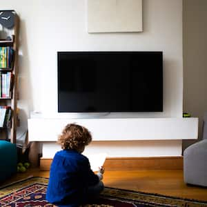 wall mounted tv in living room with small child sitting on ground 