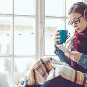 A young woman sitting by the window listening to music