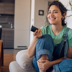 Happy woman watching tv on chair with remote