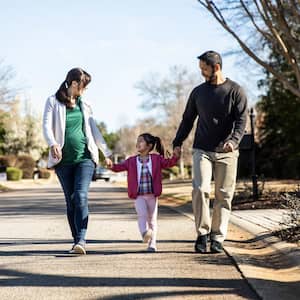 A family of three walking down a street in their neighborhood
