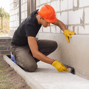 construction worker waterproofing the foundation of a house