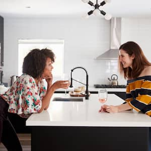 Two friends chatting in kitchen over white countertop