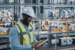 A WORKER CONSULTS A CLIPBOARD IN A FACTORY