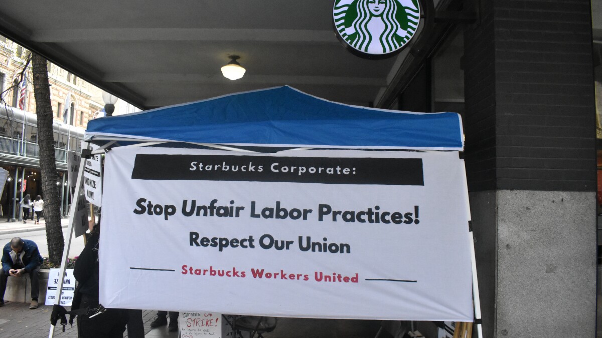 A large sign posted across a tent outside of the Starbucks on East Houston & St. Mary's. It reads "Stop Unfair Labor Practices! Respect Our Union".