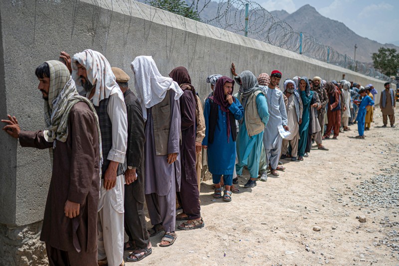 Afghan internally displaced refugee men stand in a queue to identify themselves and get cash as they return home to the east, at the United Nations High Commissioner for Refugees (UNHCR) camp in the outskirts of Kabul on July 28, 2022. - Hundreds of internally displaced Afghans who had taken refuge in the capital left for their homes in the country's eastern provinces Thursday, almost a year after the war that forced them to flee ended. (Photo by Wakil KOHSAR / AFP) (Photo by WAKIL KOHSAR/AFP via Getty Images)