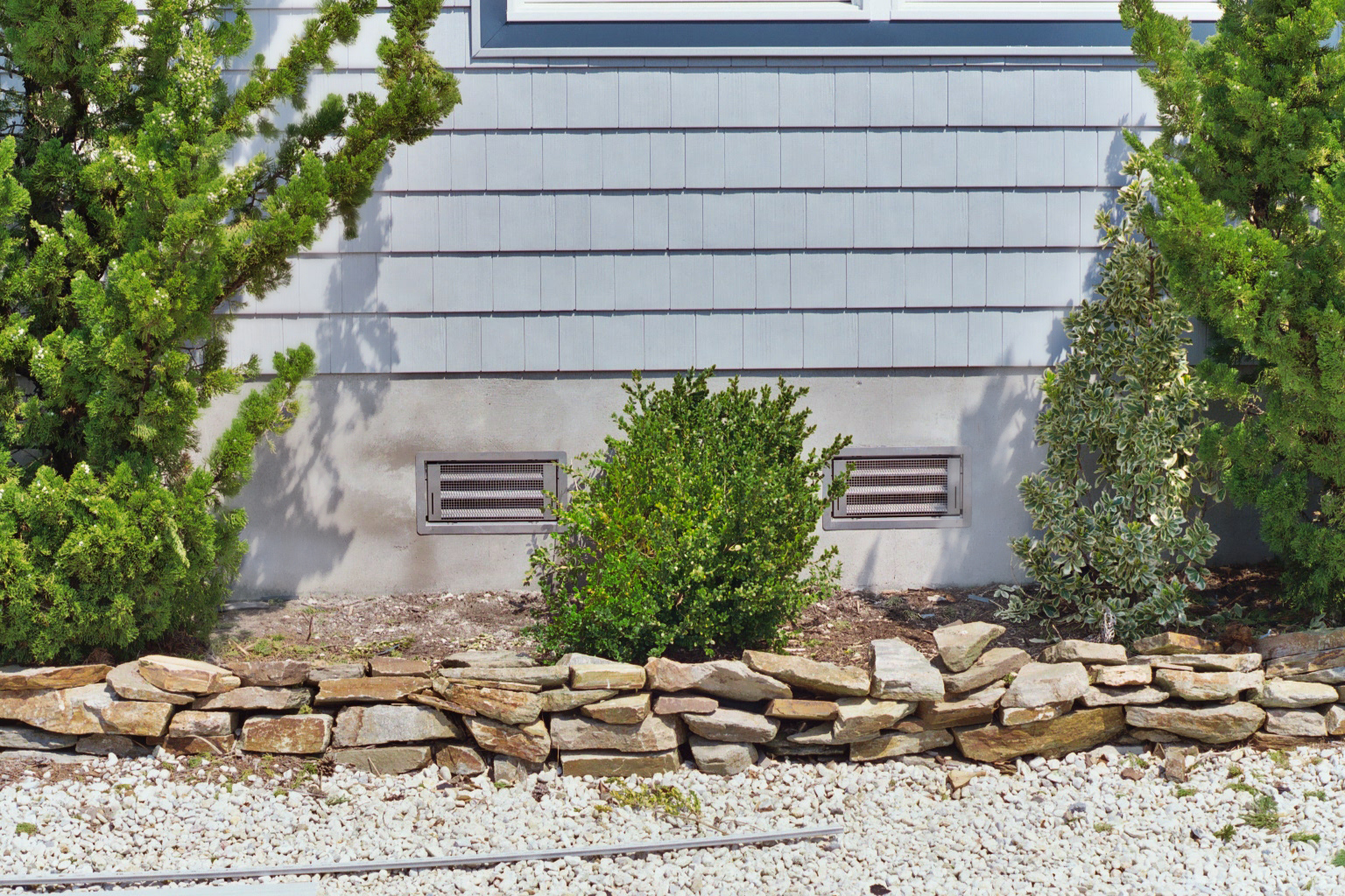 SmartVent flood vents installed on a home with bushes and rocks