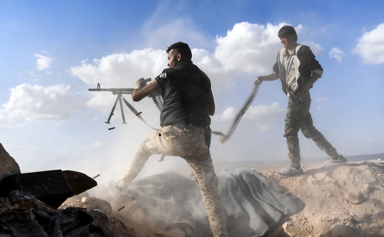 A member of the Syrian pro-regime forces fires a machine gun as a comrade holds his feeding ammunition belt on November 11, 2017. It was during an advance toward rebel-held positions west of Aleppo.