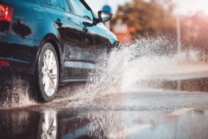 A CAR DRIVES SPLASHING THROUGH A PUDDLE