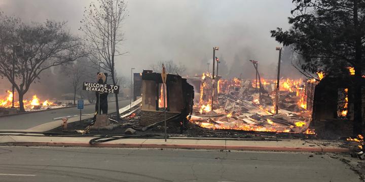 A sign saying "Welcome to Paradise" stands next to a burning building.