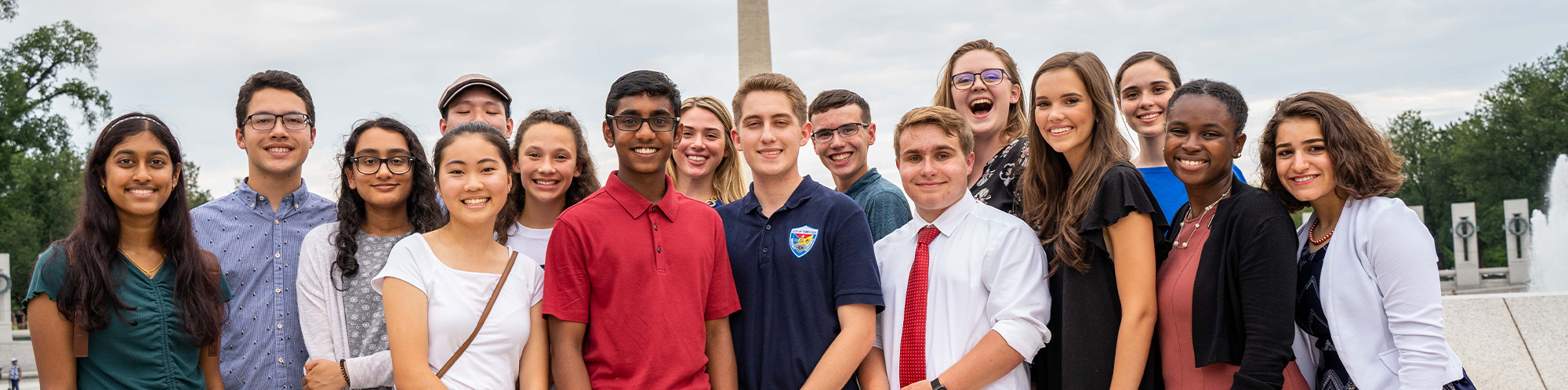 A group of teenagers stand together in front of the World War II memorial and the Washington Monument.