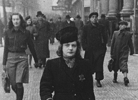 A woman walks down the street with a Jewish star visible on her coat