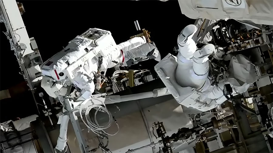 Spacewalkers Koichi Wakata and Nicole Mann wearing spacesuits are pictured installing hardware on the space station, preparing the orbiting lab for its next roll-out solar array