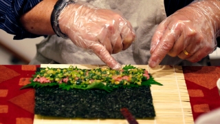 Person putting food on a seaweed wrap.