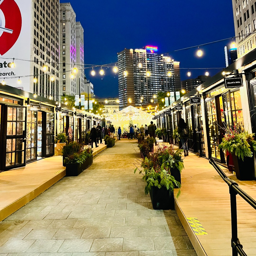 Downtown Detroit Market shops lit up by white lights as the sky darkens above.