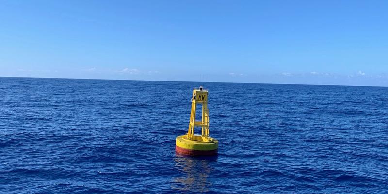 A yellow buoy with a red base floats in the sea under a blue sky. 