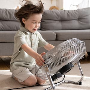 A little boy sitting on the floor in front of a big fan