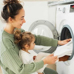 Mother and girl loading washing machine