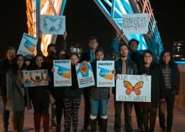 A group of young people stand in the middle of the street on a bridge while holding protest posters