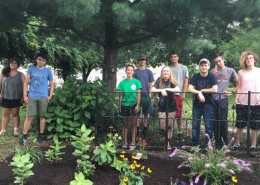 A group of young people stand behind a pollinator garden