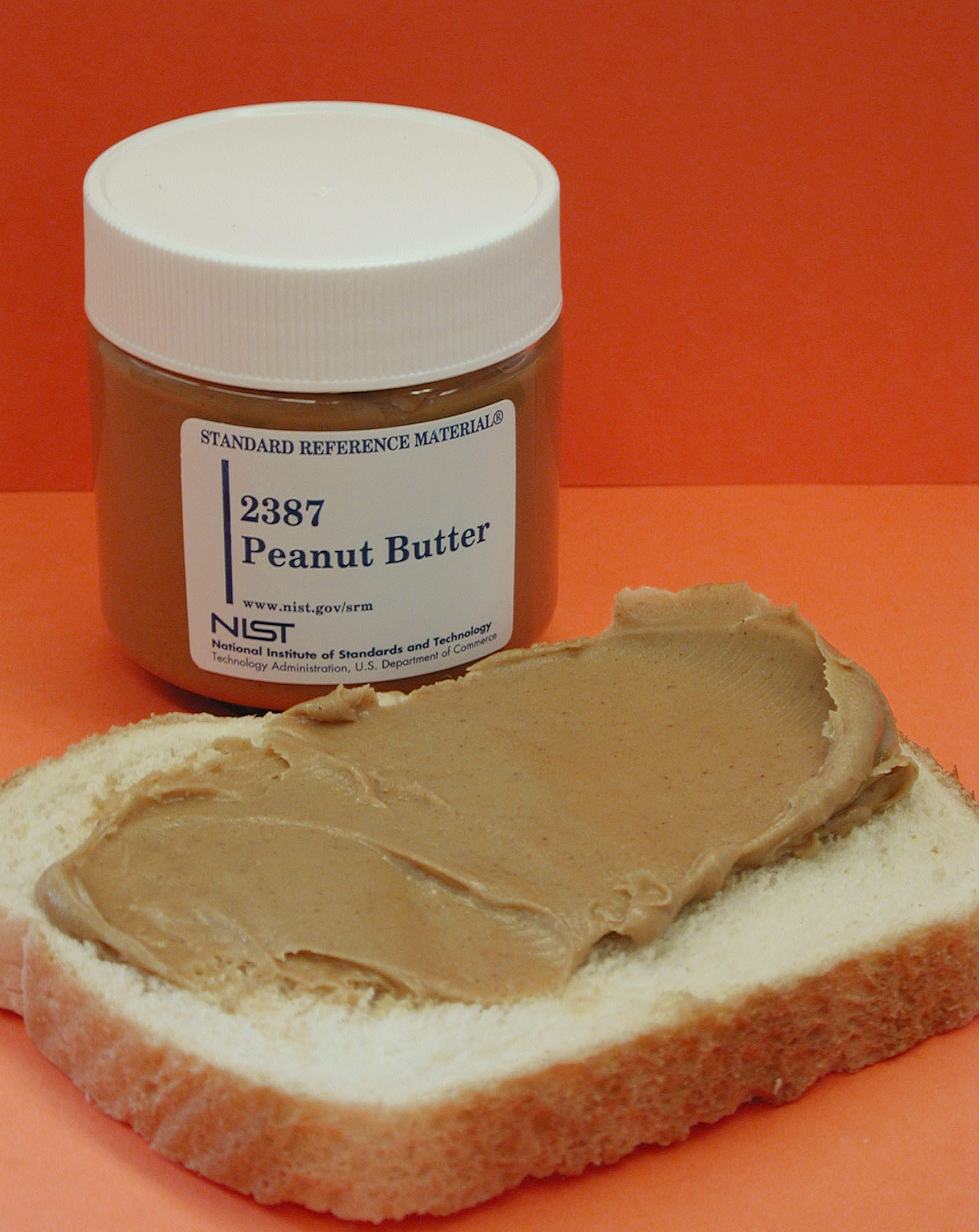 Peanut butter spread across a slice of bread, next to a jar of NIST standard reference material for peanut butter.