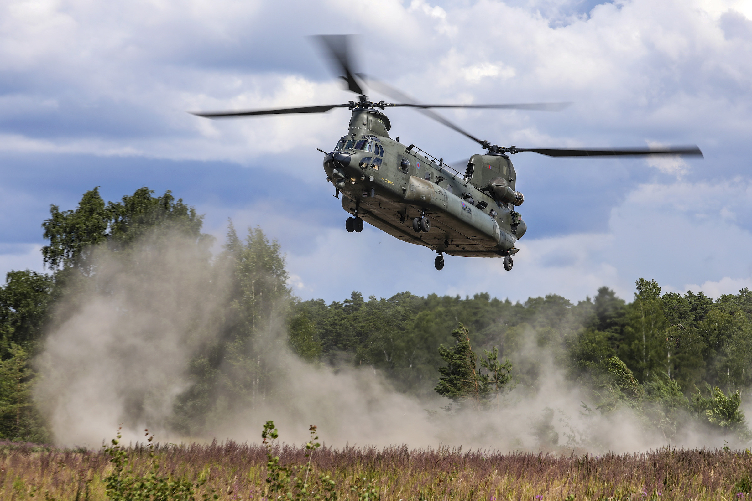 A Chinook helicopter sprays up dust as it lands in an open plain.