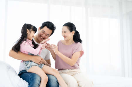 Happy asian family with daughter playing together at home. parents are having fun on the bed Фото со стока