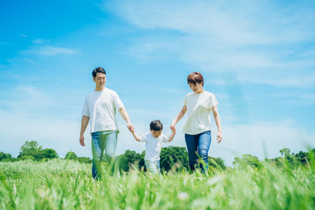 Parents and their child holding hands and walking in a sunny green space on fine day