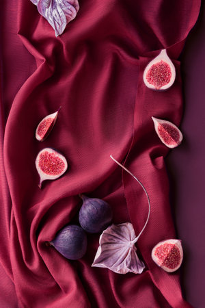 Fresh halved fig fruits and metallic cala flower on vine red silk textile background.
