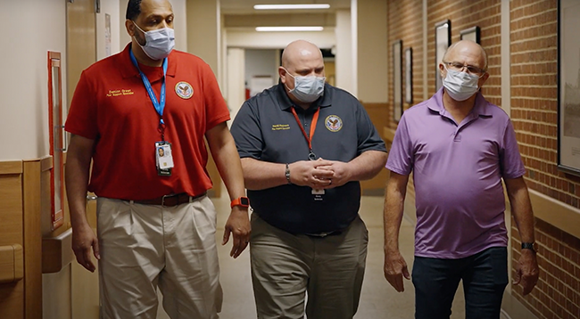 Image which shows VA staff and Veteran walking down hallway