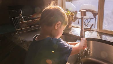 Little boy washes hands at kitchen sink, winter scene thru windows