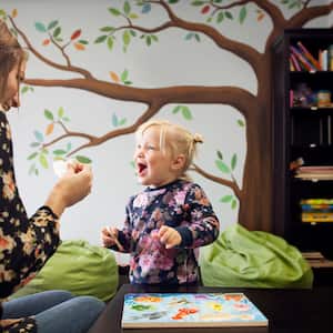 A mother playing with her daughter in playroom with mural on wall