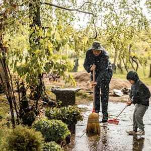 A father and son sweeping water from front yard on rainy day