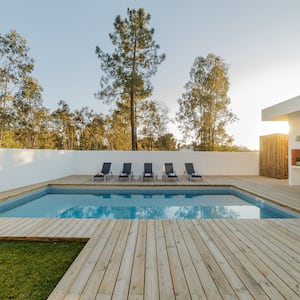 a light wood pool deck surrounding a square pool, with five deck chairs and grass