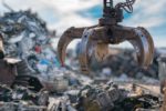 AN INDUSTRIAL CLAW GRABS SCRAP STEEL FROM A GIANT OUTDOOR PILE OF JUNKpg