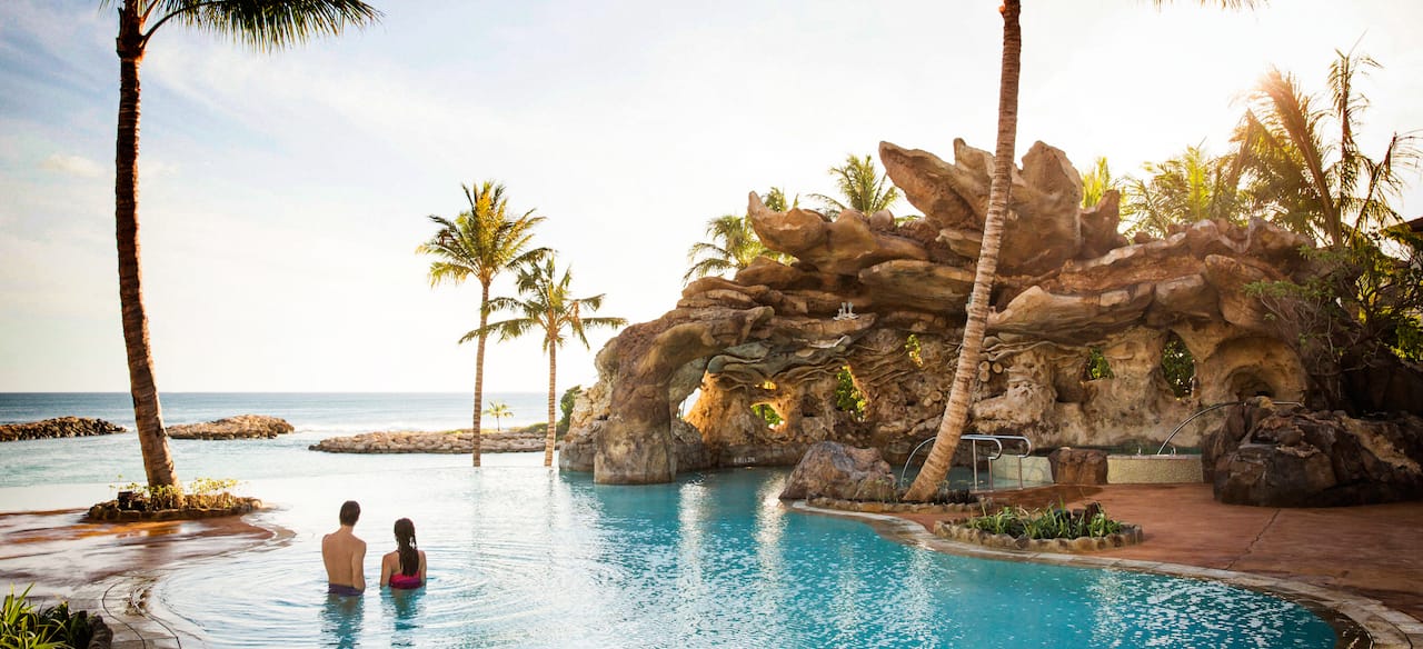 A couple unwinds in the waters of the Ka Maka Grotto oceanfront pool while looking out to the ocean