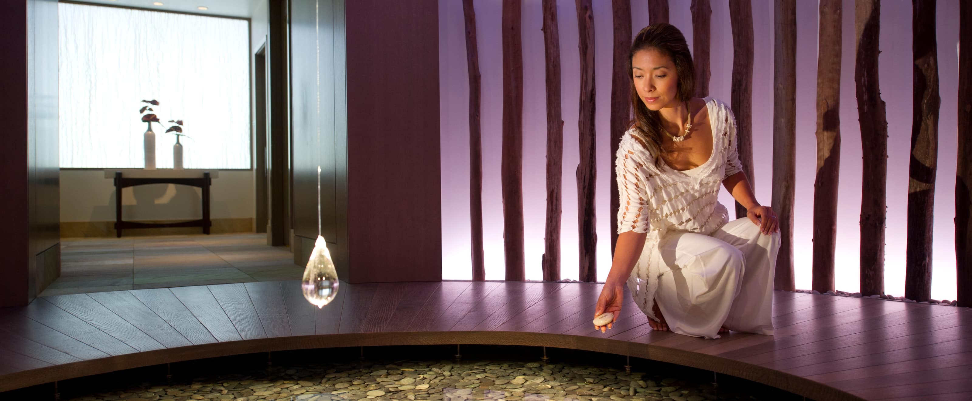 A woman crouches beside the stone-filled affirmation pond inside Laniwai, about to drop another stone in