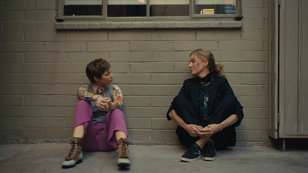 Hollywood Stargirl | First Look Photo | Image of Stargirl Caraway (actor Grace VanderWaal) and Roxanne Martel (Uma Thurman) sitting on the ground together.