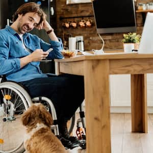 man in wheelchair next to dog at kitchen table