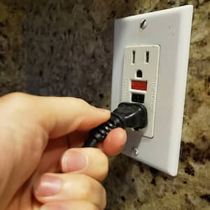 human hand of a man plugging an electrical cord into a GFCI electrical outlet