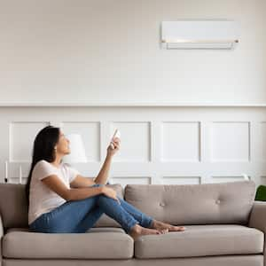 woman on couch using remote to adjust air conditioner