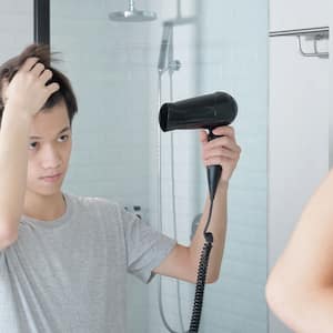 Young man using hair dryer in front of the mirror