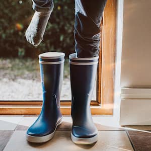 Child putting on rain boots on tile floor