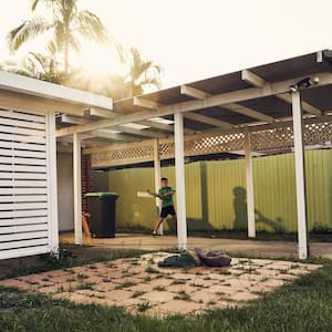 Boy hitting a ball in backyard under carport