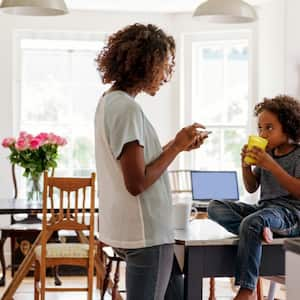 A mother using smartphone while her son is drinking milk