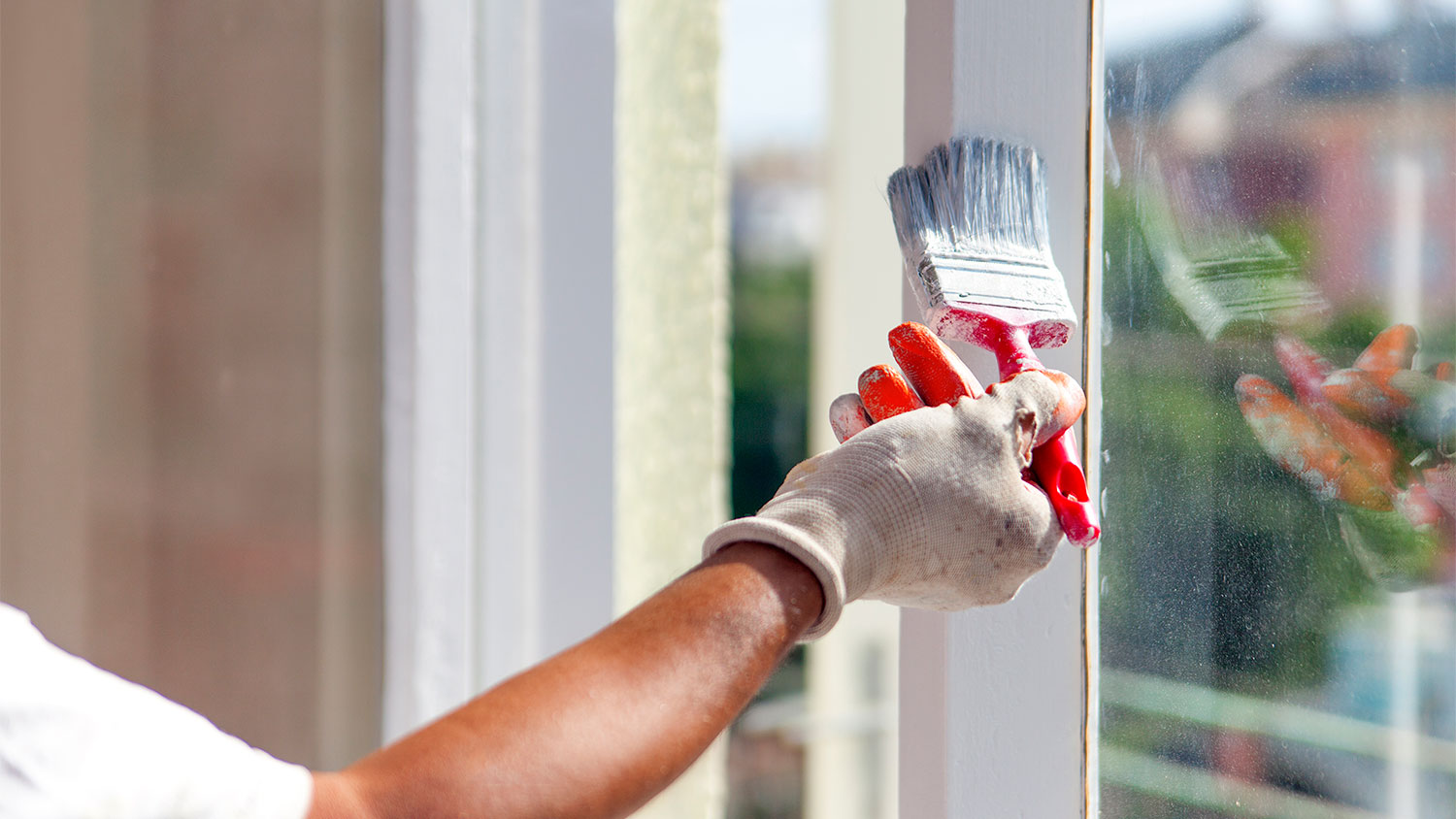 A closeup of a man painting window trim